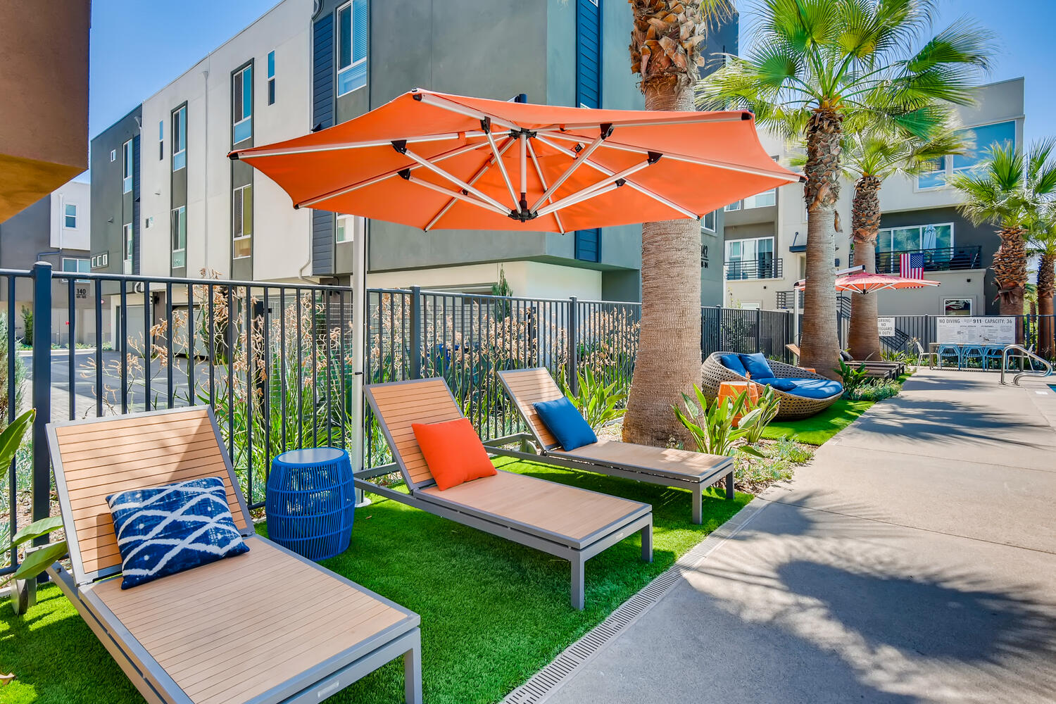 Outdoor pool area with blue and white striped pillows, lounge chairs, and a large orange umbrella.