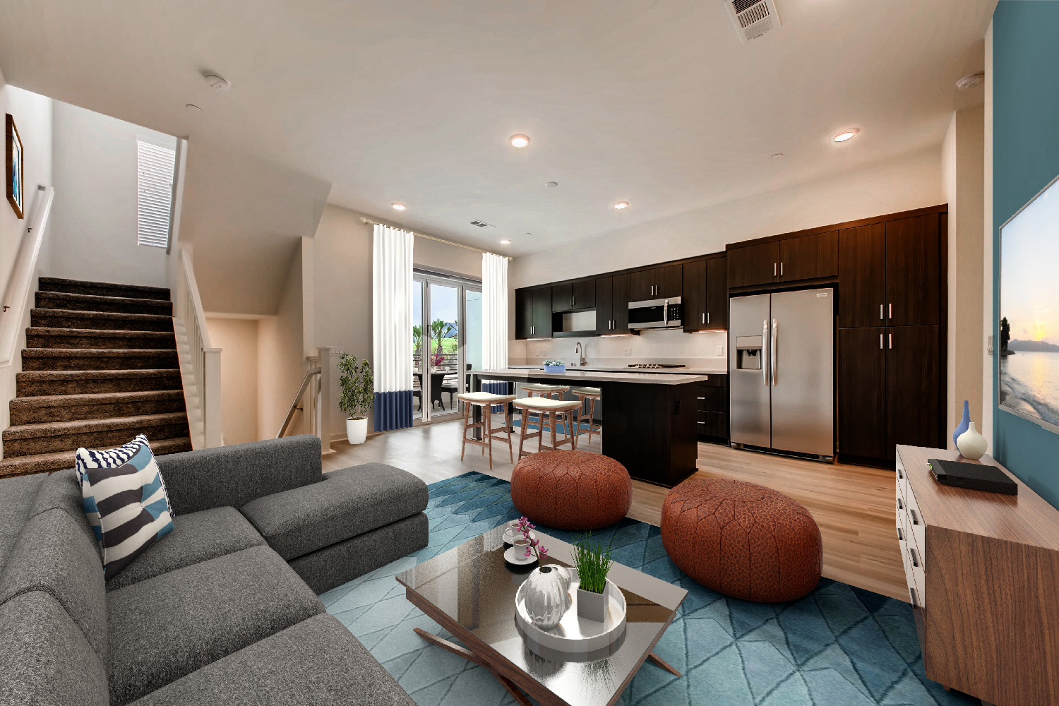 modern living room and kitchen with a gray sofa, blue and white throw pillows, dark wood cabinets, and a beach painting.